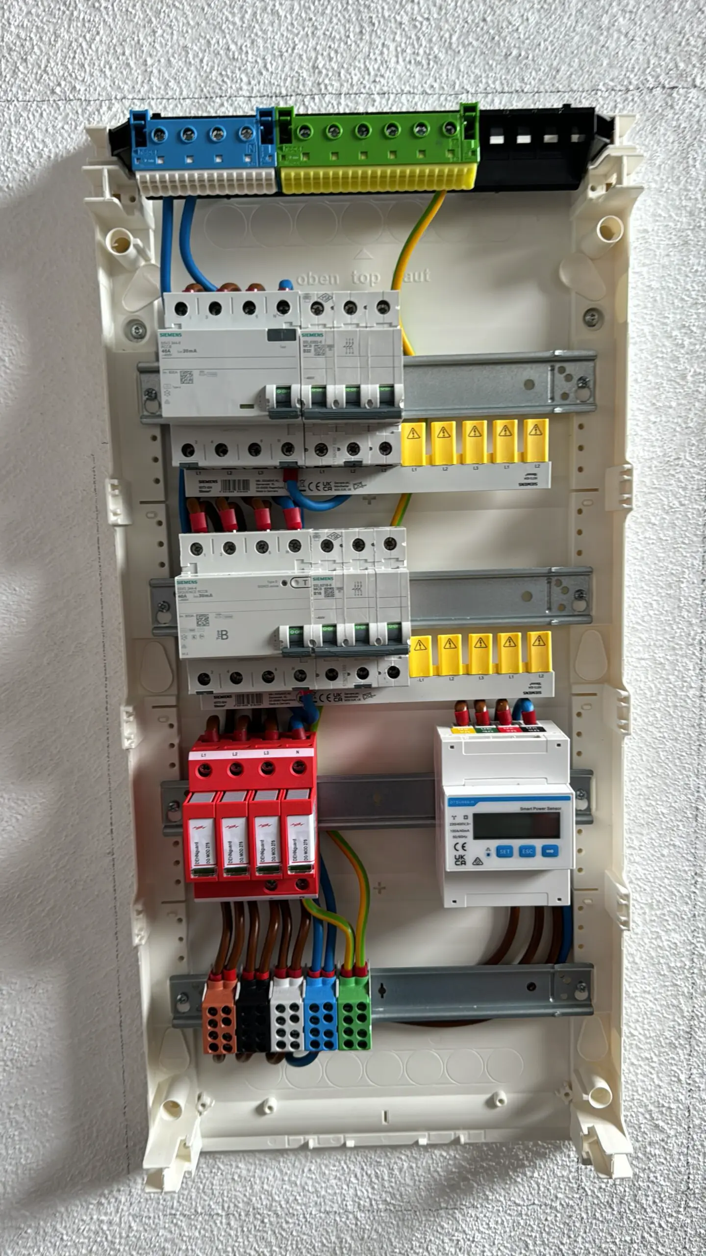 Verteilerkasten mit bunten Kabeln von Innen an der Wand.